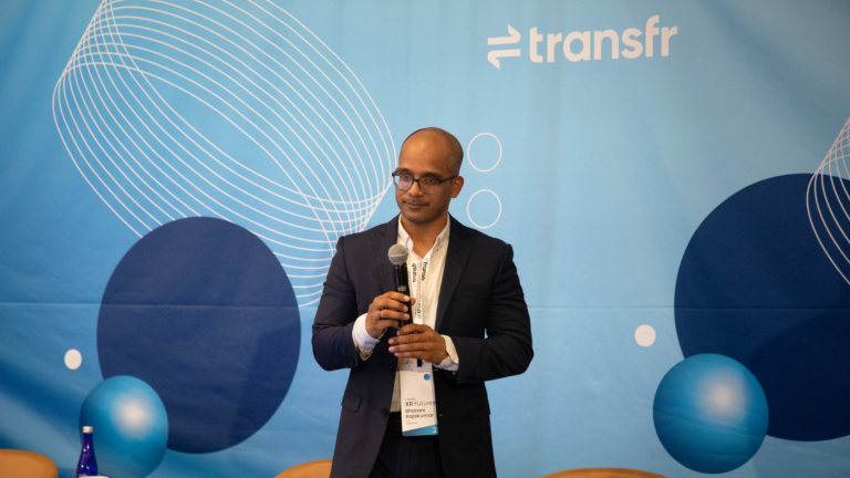 Transfr CEO Bharani Rajakumar in front of a blue Transfr background.